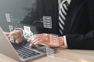 Foto: Mann vor Laptop mit schwebendem digitalen Brief über der Tastatur